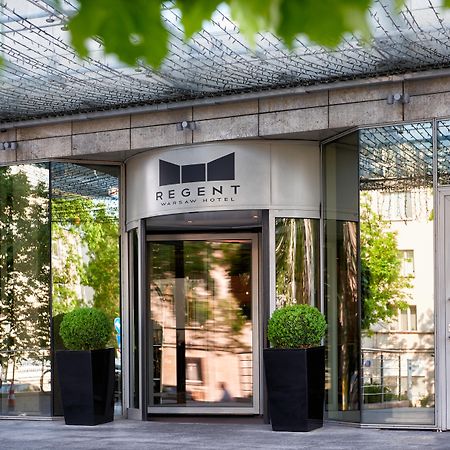 Regent Warsaw Hotel Exterior foto The photo shows the entrance of a building with a modern design. The main feature is a revolving door with a sign above it that reads "REGENT." The entrance is flanked by large potted plants, and the facade consists of glass and reflective surfaces, 