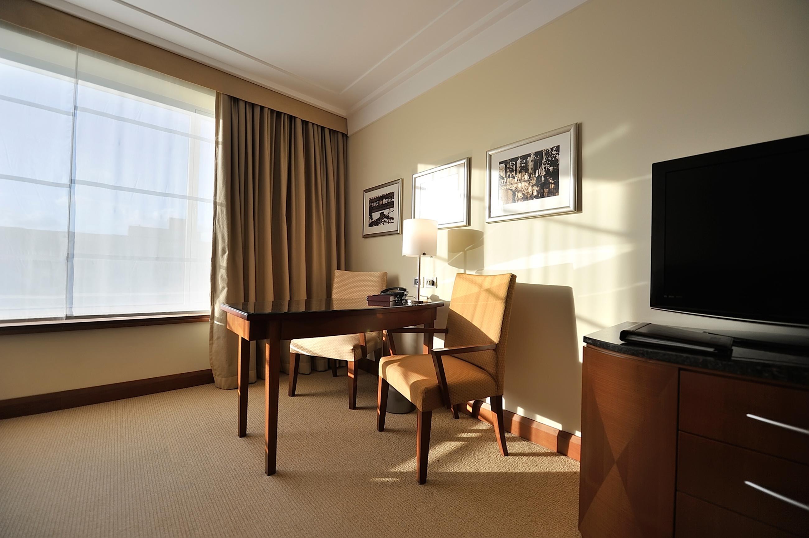 Regent Warsaw Hotel Exterior foto The photo shows a well-lit hotel room or office space. On one side, there is a large window with light-colored curtains that allow natural light to enter. Near the window, there are two upholstered chairs, one of which is positioned at a wooden desk.
