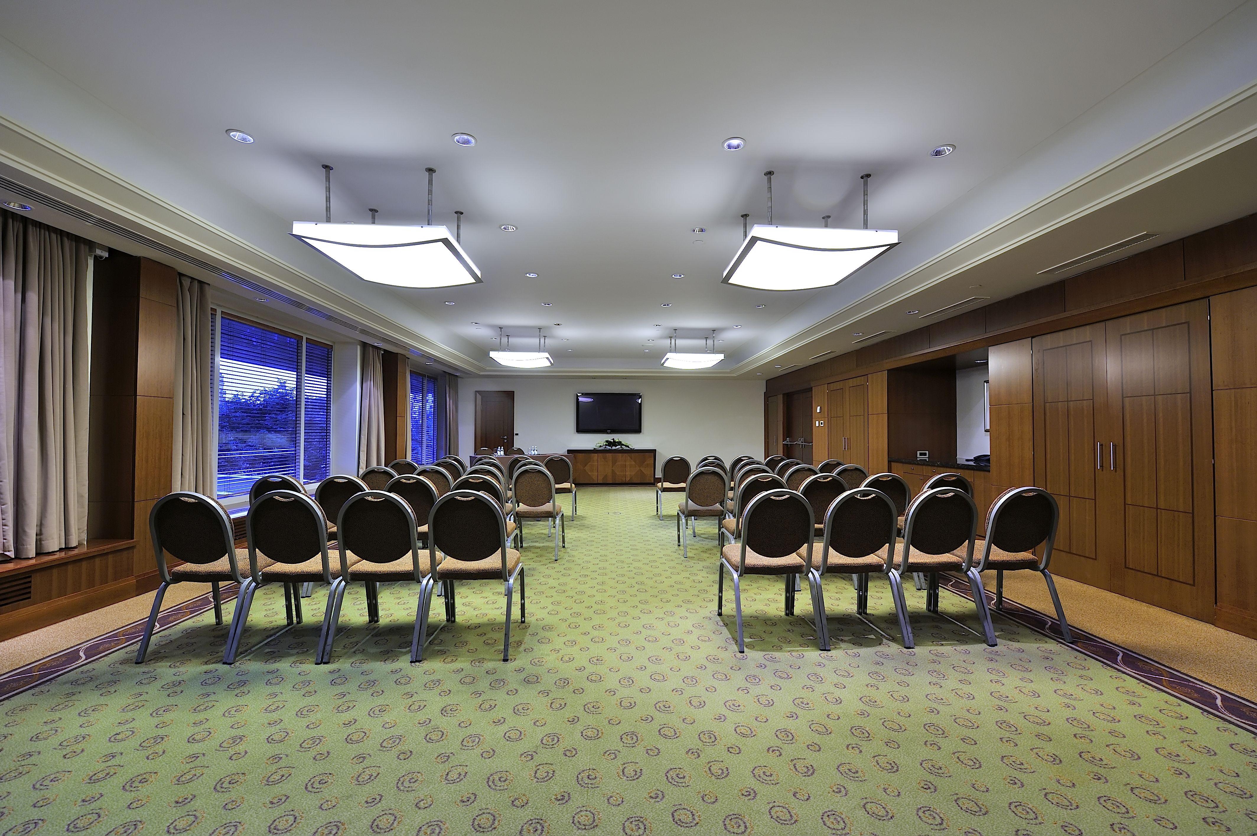 Regent Warsaw Hotel Exterior foto The photo shows a conference room or meeting space. It features several rows of chairs arranged in a semi-circle facing a wall-mounted television. The room has a carpeted floor with a patterned design and is illuminated by rectangular ceiling lights.