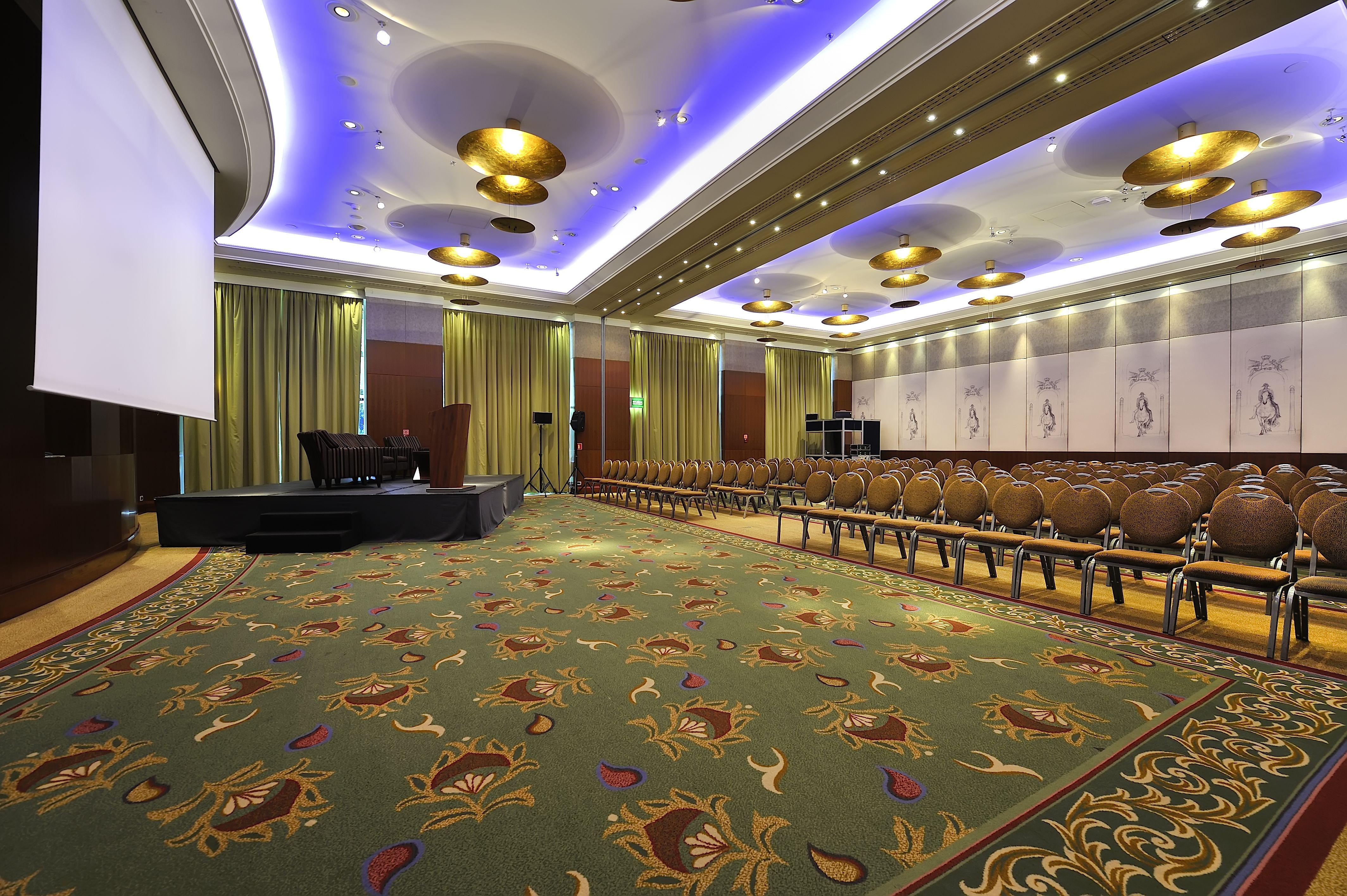 Regent Warsaw Hotel Exterior foto The photo depicts a spacious conference room or event space. The room features a decorative carpet with floral patterns and is arranged with rows of elegant, cushioned chairs. At the front of the room, there is a low platform or stage with seating, p