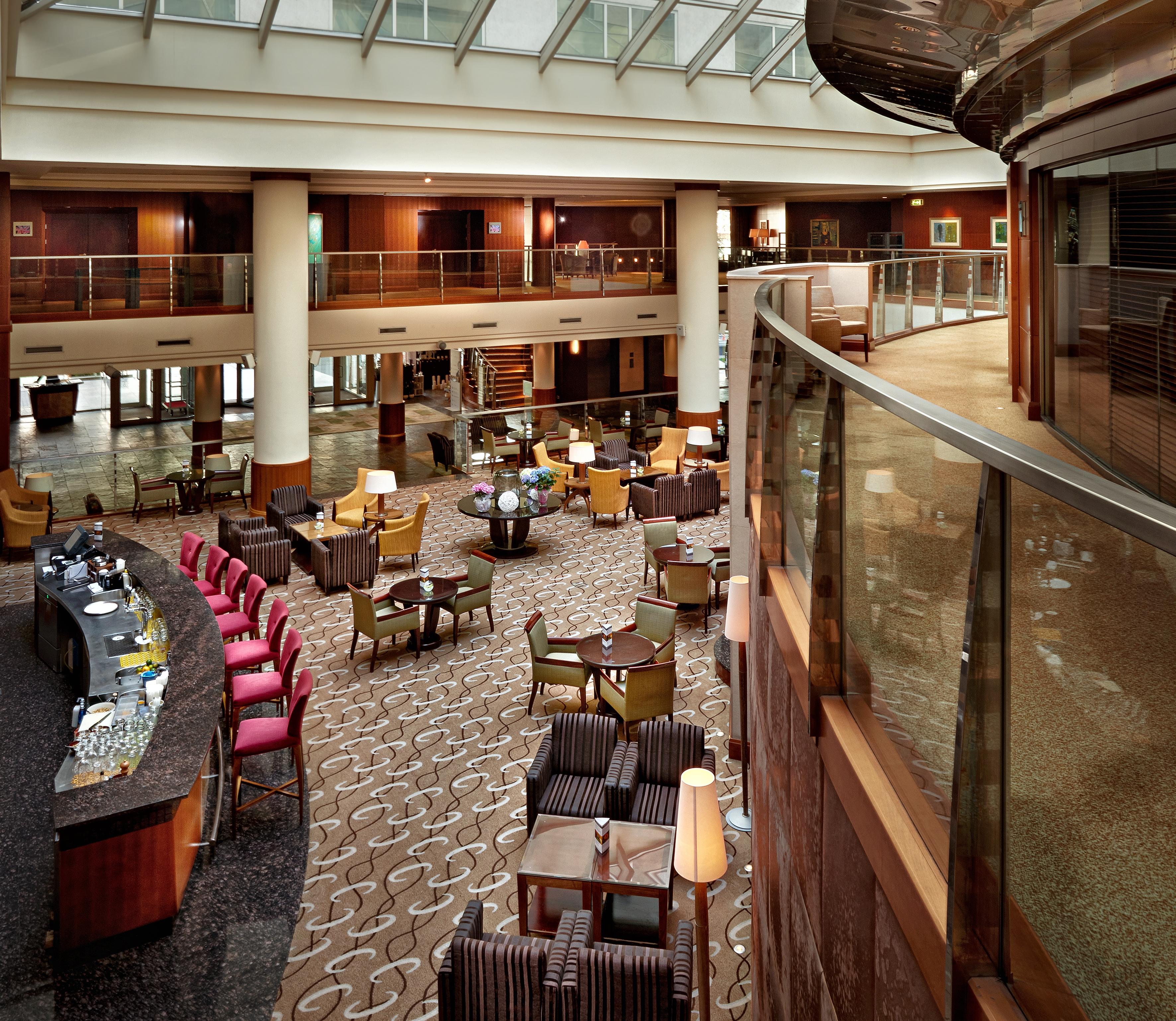 Regent Warsaw Hotel Exterior foto The photo shows the interior of a hotel lobby or lounge area. There are various seating arrangements with comfortable chairs and small tables. The layout appears open and spacious, with a curved balcony or walkway above. In the foreground, there is a