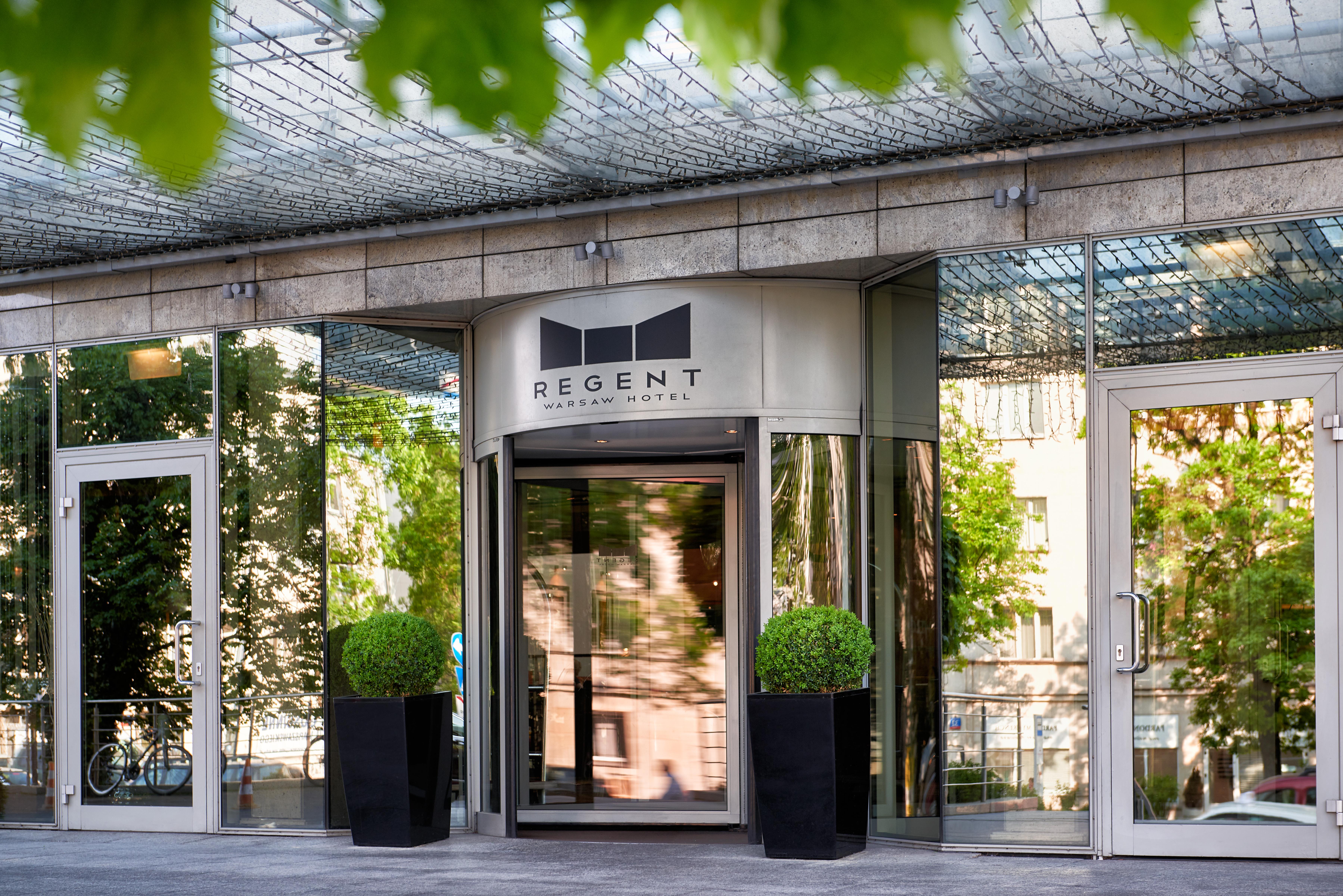 Regent Warsaw Hotel Exterior foto The photo shows the entrance of a building with a modern design. The main feature is a revolving door with a sign above it that reads "REGENT." The entrance is flanked by large potted plants, and the facade consists of glass and reflective surfaces, 