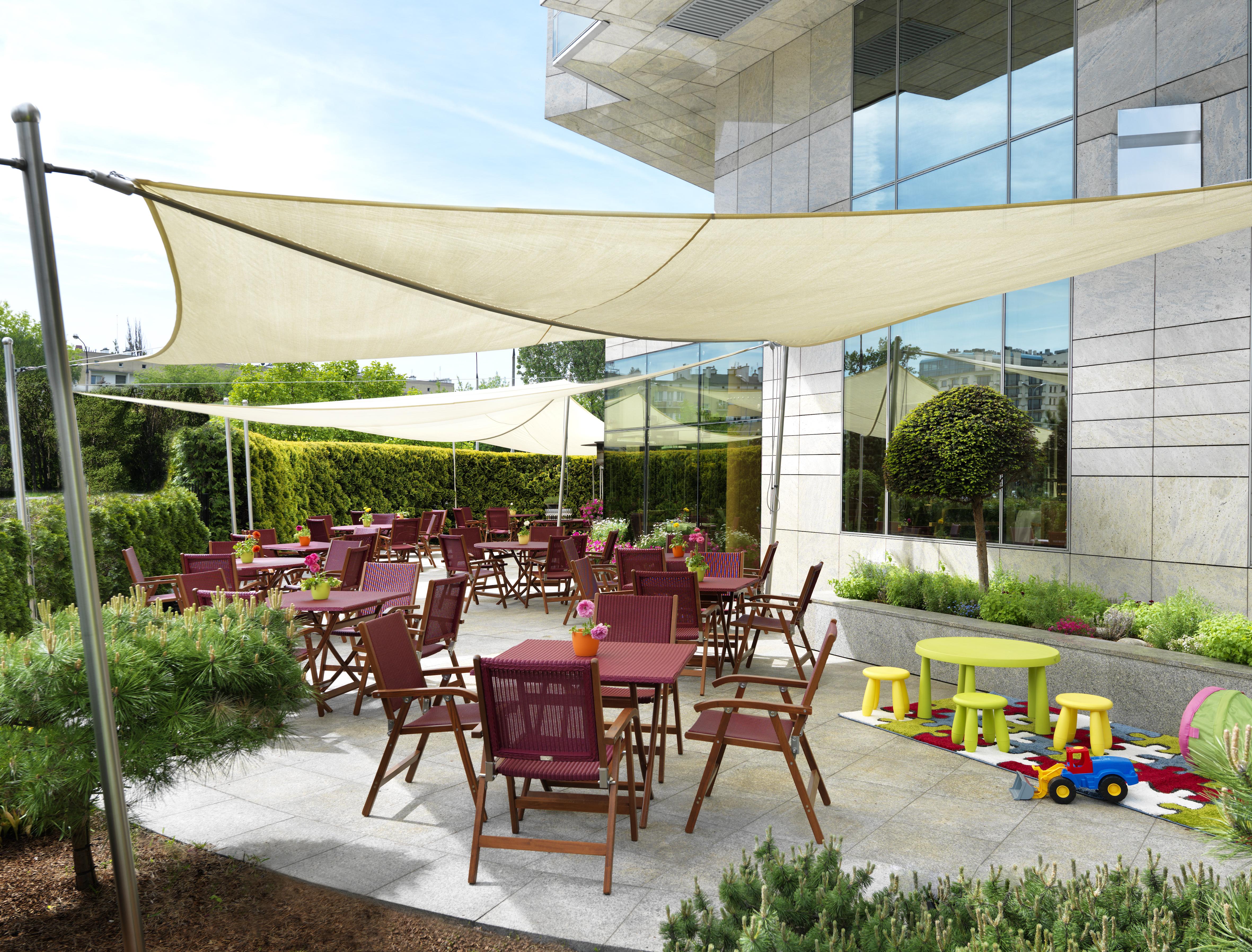Regent Warsaw Hotel Facilități foto The photo shows an outdoor dining area with a modern design. There are several wooden tables and chairs arranged on a paved surface, with some tables set for dining. Above the seating area, there are large fabric canopies providing shade. In addition