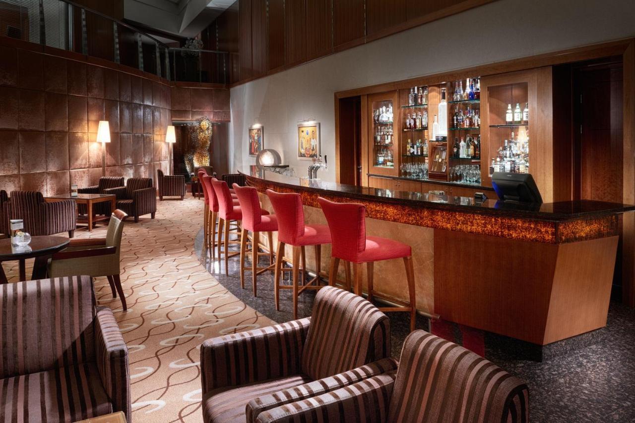 Regent Warsaw Hotel Exterior foto The photo shows a stylish and sophisticated bar interior. There are several tall bar stools with red upholstery positioned along a polished wooden bar counter. Behind the bar, shelves display a variety of bottles and glassware, indicating a well-stoc