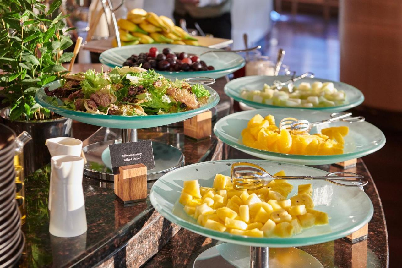 Regent Warsaw Hotel Exterior foto The photo displays a buffet-style setup featuring a variety of food items. There are several glass trays stacked on a countertop, each holding different types of food. 

1. **Fresh Vegetables and Fruit:** One tray appears to have a mix of leafy green