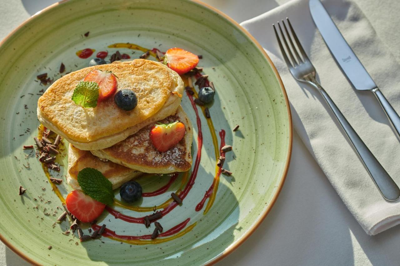 Regent Warsaw Hotel Exterior foto The photo shows a plate of pancakes stacked on top of each other. The pancakes are garnished with fresh strawberries, blueberries, and mint leaves. There are drizzles of syrup and chocolate around the pancakes, adding a colorful touch to the presenta