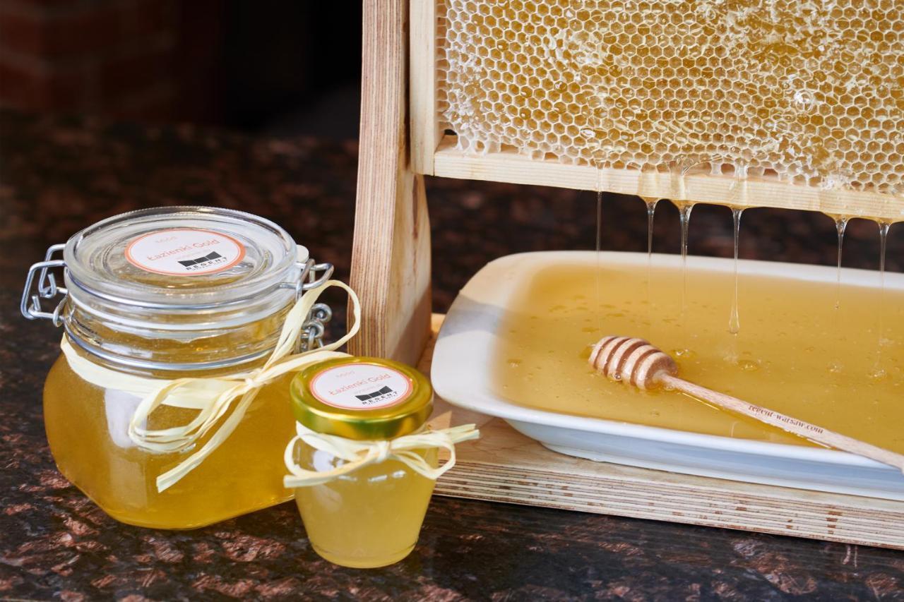Regent Warsaw Hotel Exterior foto The photo shows a display of honey products. There is a honeycomb structure from which honey is dripping into a small plate. A wooden honey dipper rests on the plate, which contains liquid honey. Additionally, there are two jars of honey: one larger 