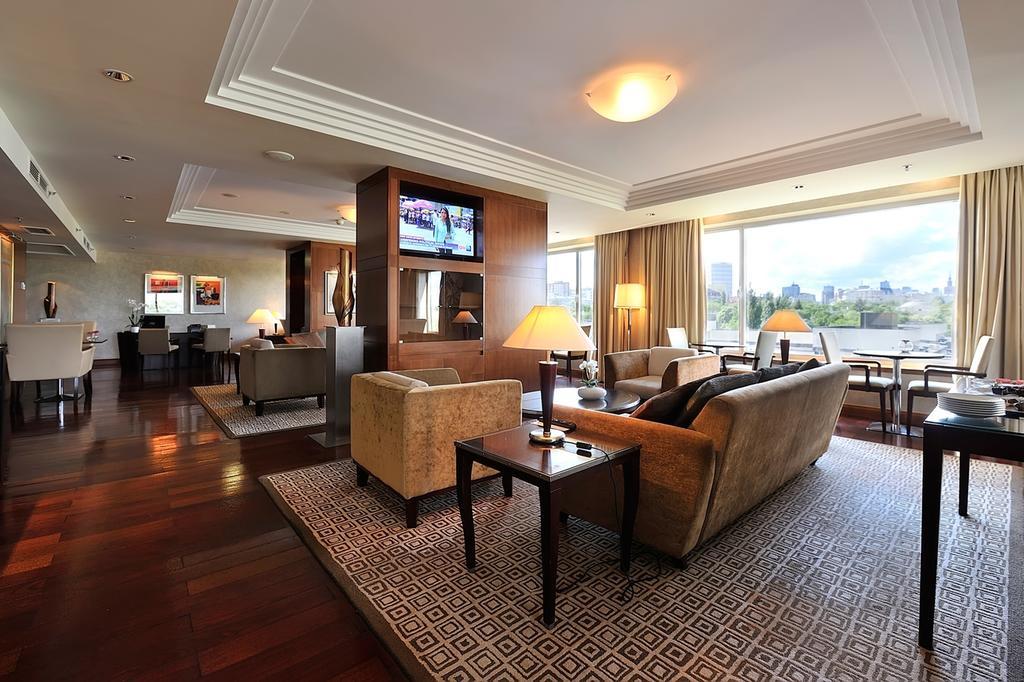 Regent Warsaw Hotel Exterior foto The photo showcases a spacious and elegantly designed living area. It features two comfortable sofas, a coffee table, and floor lamps that create a warm ambiance. There's a large flat-screen television mounted on the wall. The room has large windows 
